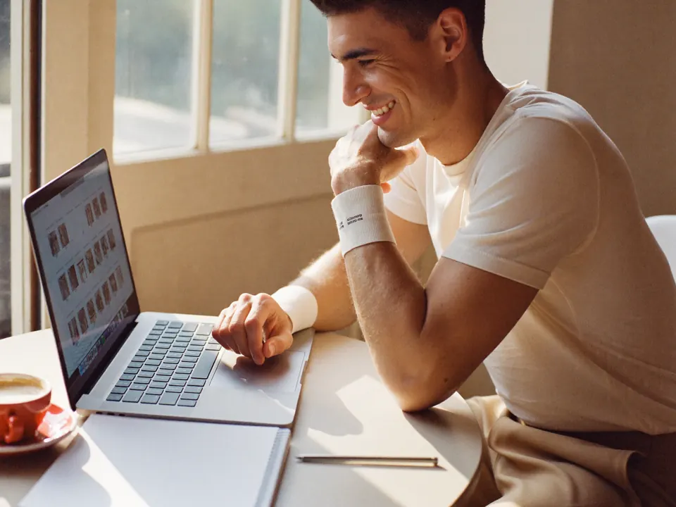 A young man smiling at his laptop at a café table